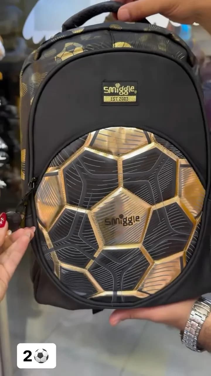 کوله پشتی اسمیگل Smiggle، رنگ مشکی و طلایی، جنس چرم مصنوعی، طرح هندسی و لوگو، کوله پشتی مدرسه
