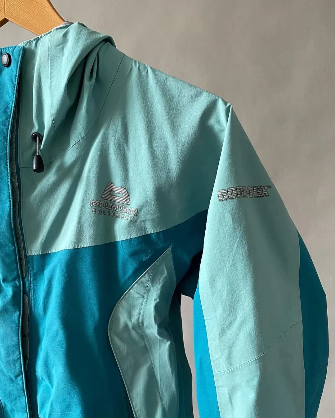 کاپشن گورتکس تک لایه زنانه Mountain Equipment، رنگ سبز آبی و آبی، کلاهدار زیپدار