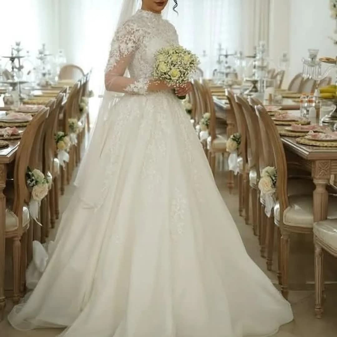لباس عروس کار دست دنبالهدار مزون آراد، رنگ سفید، جنس توری، طرح گلدوزی، بلند، یقه بسته، آستین بلند، پفدار