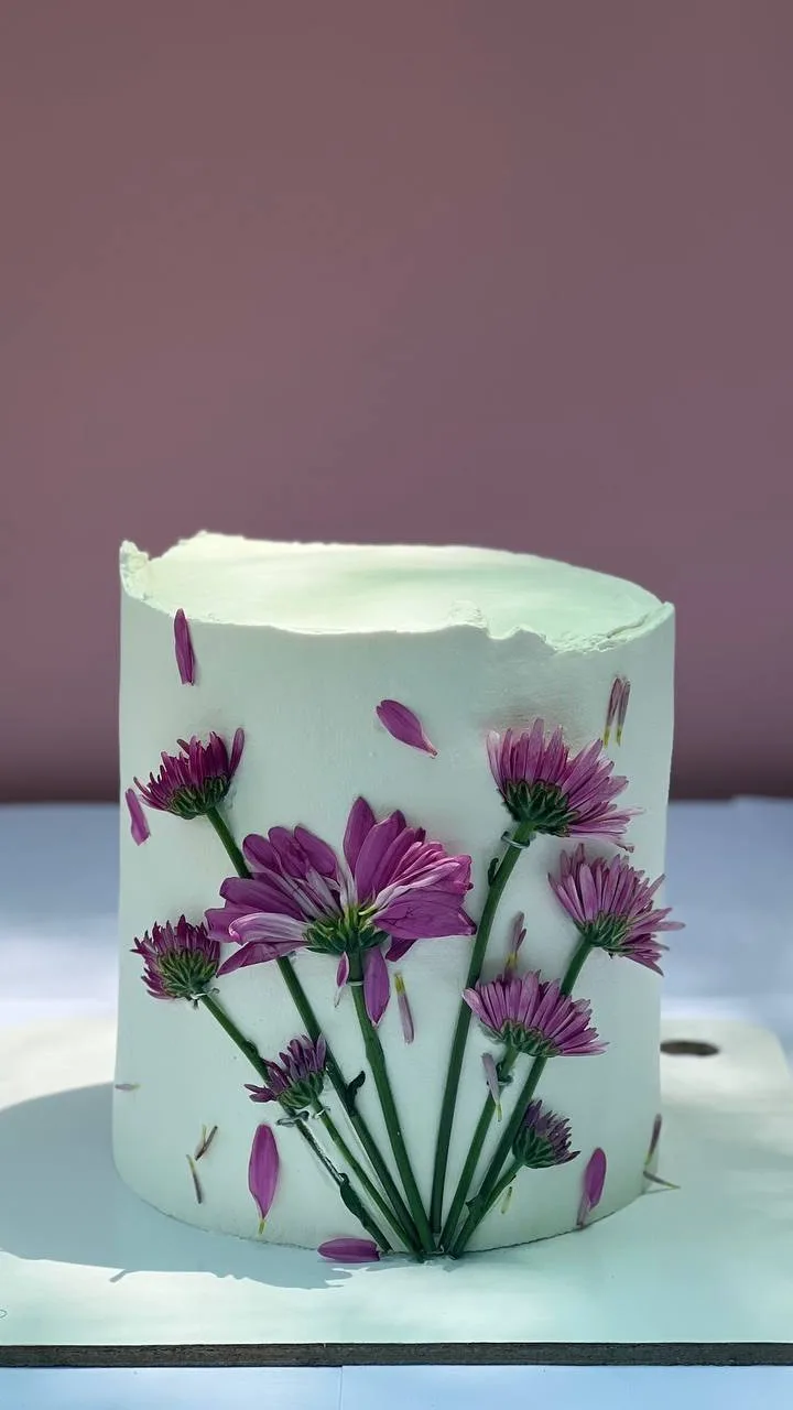 کیک تولد با تزیین گل، رنگ سفید، بنفش و سبز، طرح گلدار، استوانه‌ای، تزیین شده با گل