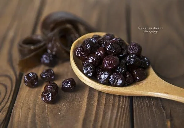 آلبالو خشک، رنگ قهوه‌ای و سیاه، جنس چوب، قاشق چوبی پر از آلبالو