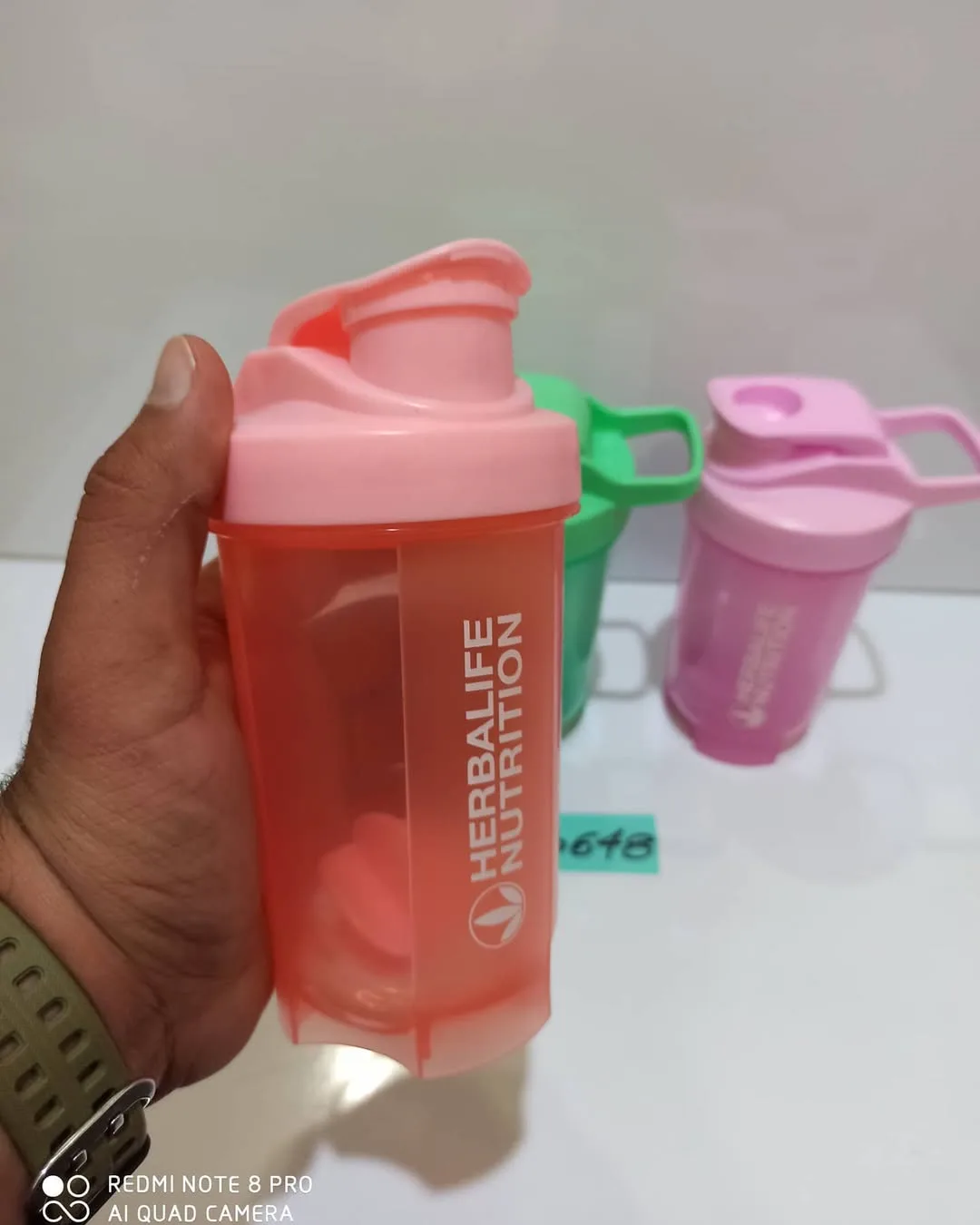 شیکر هربالایف، رنگ صورتی و گلبهی، جنس پلاستیک، استوانهای درب پیچی ضامندار