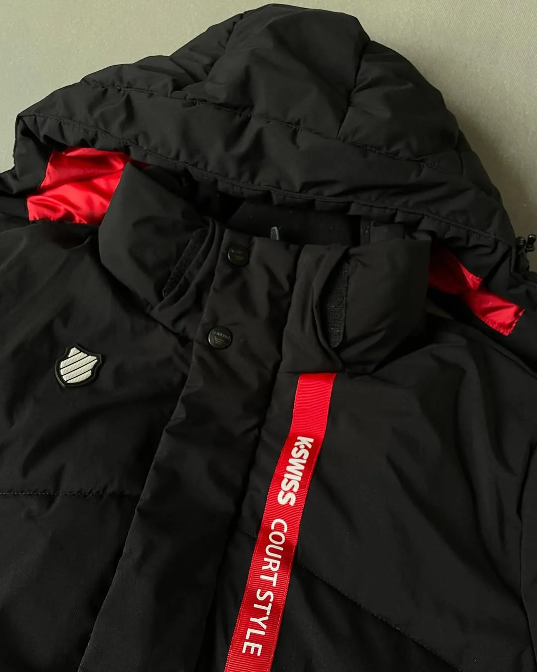 کاپشن الیاف کلاهدار K-Swiss، رنگ مشکی و قرمز، جنس پلاستیک، کلاه‌دار کوتاه